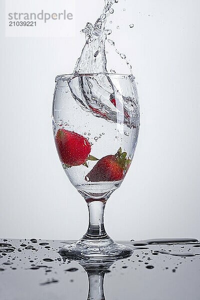 Two strawberries dropped in a water glass against a white background