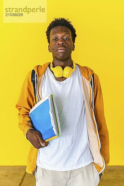 Studio portrait with yellow background of an african student standing serious