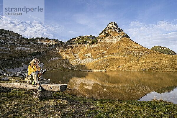 Lake Augstsee and the Atterkogel mountain on the Loser. A hiker sits on a bench and reads a book. Autumn  good weather  blue sky. Altaussee  Bad Aussee  Ausseer Land  Totes Gebirge  Styria  Upper Austria  Austria  Europe