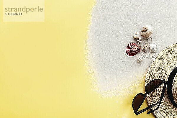 Summer background conceptual flat lay with sand  shells  straw hat and sunglasses on yellow background.