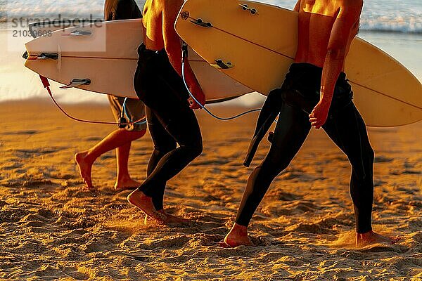 Two men are walking on the beach with surfboards. The surfboards are yellow and white. The beach is sandy and the sky is orange