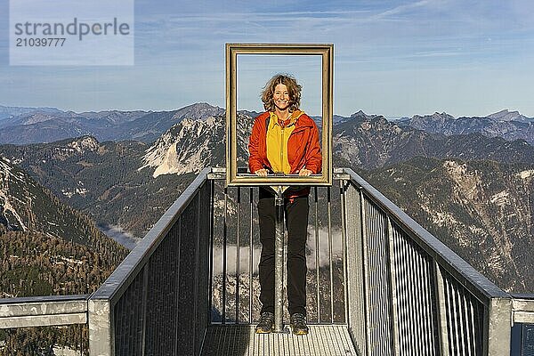 A hiker stands on the 5fingers viewpoint and looks through the picture frame. View from the Dachstein Krippenstein. Autumn  good weather. Some clouds in the mountains. Lake Hallstatt  Salzkammergut  Upper Austria  Austria  Europe