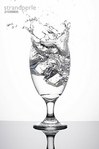 A studio photo of ice being dropped into a glass of water against a white background