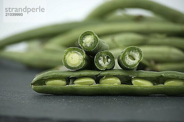 Heap of cut green beans on black stone table over white background. Organic and diet food