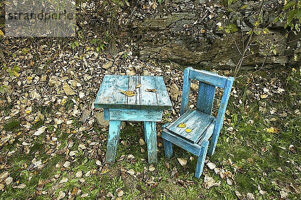 An old blue wooden table and chair stand empty in grass during autumn in north Idaho