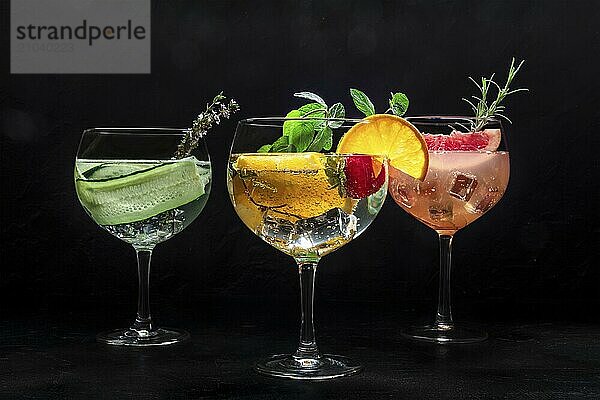 Fancy cocktails with fresh fruit. Gin and tonic drinks with ice at a party  on a black background. Alcohol with cucumber  orange  rosemary  mint