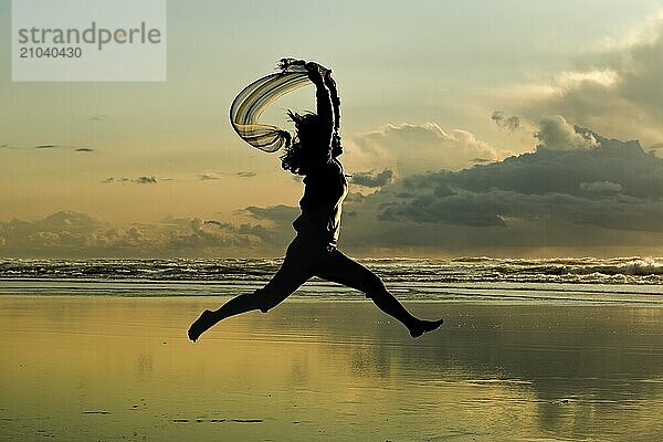 A woman with a scarf leaps on the beach in Newport  Oregon