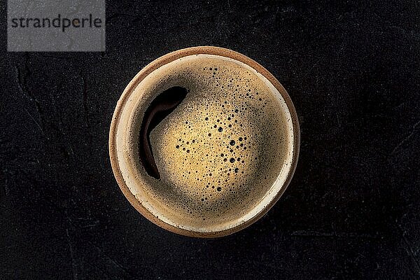 A cup of black coffee with froth  a close-up  overhead flat lay shot on a black background  Food photography