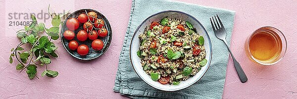 Quinoa tabbouleh salad in a bowl panorama  a healthy dinner with tomatoes and mint  overhead flat lay shot with a drink on a pink background