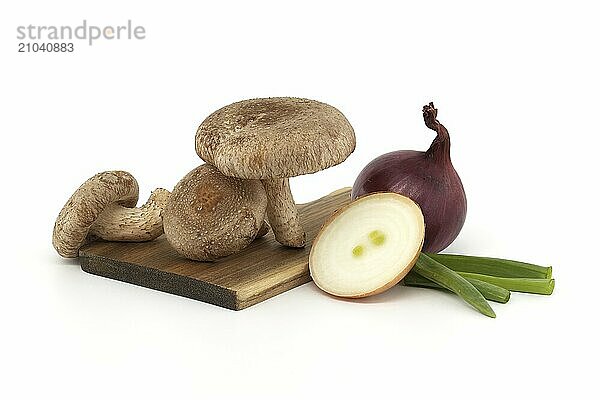 Shiitake mushrooms and various onions on a wooden cutting board isolated on white background. Recipes and medicinal herbs