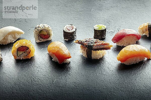 Sushi on a black slate plate. Nigiri with eel  salmon and tuna  roll with avocado and maki with cucumber on a black background  with copy space  Food photography