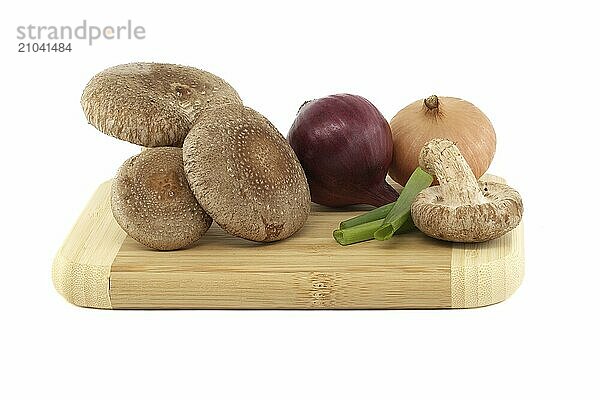 Shiitake mushrooms and various kinds of onions on a wooden cutting board over on white background. Recipes and medicinal herbs