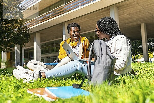 African american students studying with laptop together sitting in the grass outside the campus