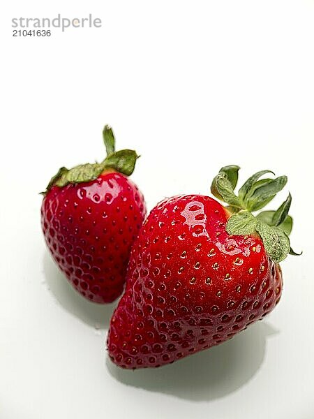 A close up photo of two ripe straberries against a white background