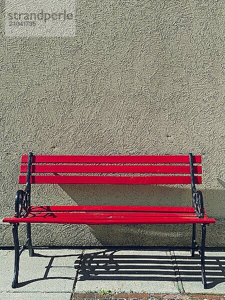 A bright red empty park bench sits against a solid wall on a sunny day in Cashmere  Washington