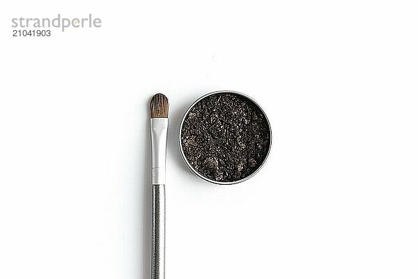 Dark brown face shadow in container and eye shadow or make-up brush. Makeup concept flat lay on white background