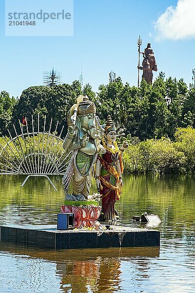 Statues of three deities of Hindi Hindu religion Hinduism left in front elephant god Ganesha right behind goddess Parvati woman of Lord Shiva stand on pedestal in holy lake Ganga Talao  in the background god Shiva  crater lake Grand Bassin  Ganga Talao  Le Petrín  Mauritius  Africa