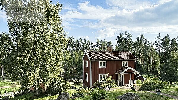 A typical red and white swedish house in smalland. green meadow in foreground  small forest in background. Blue sky with small clouds. Scandinavia landscape photo