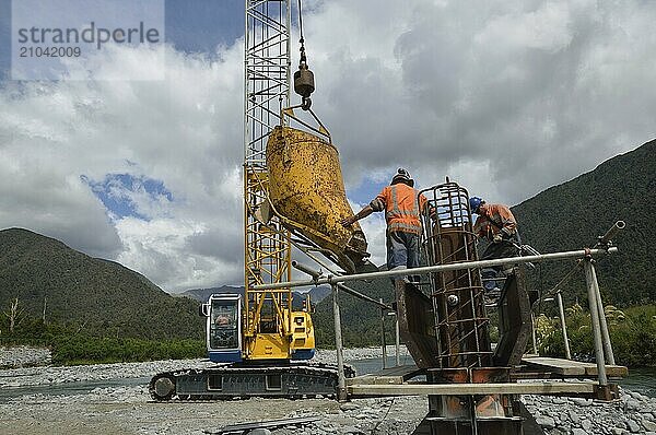 Builders pour concete into the pylon of a concrete bridge over a small river in Westland  New Zealand  Oceania