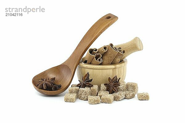 Star anise in a wooden spoon  wooden mortar filled with cinnamon sticks and brown sugar cubes isolated on white background