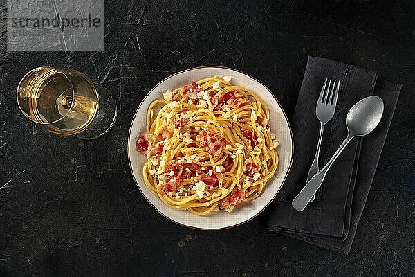 Carbonara pasta dish  traditional Italian spaghetti with pancetta and cheese  overhead flat lay shot with wine  a fork  and a spoon  on a black background  Food photography  Food photography