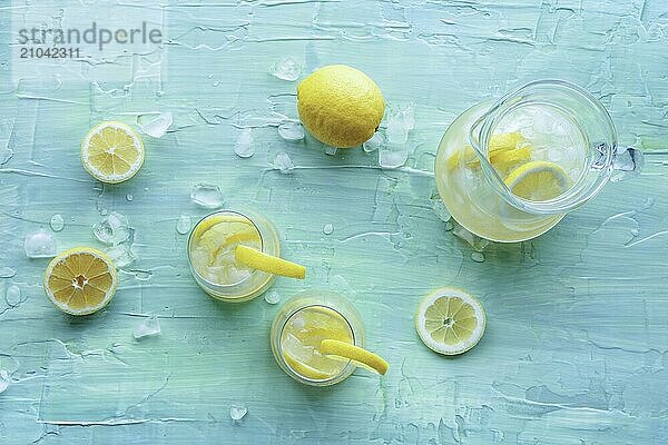 Lemonade. Lemon water drink with ice. Two glasses and a pitcher on a blue background  overhead flat lay shot. Detox beverage. Fresh homemade cocktail