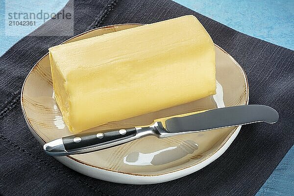 A stick of fresh butter with a knife on a plate  on a blue background  cooking ingredient