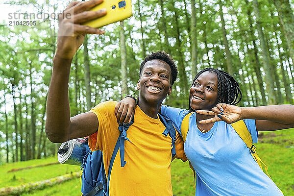 Happy young african friends gesturing success while taking selfie together in a green forest