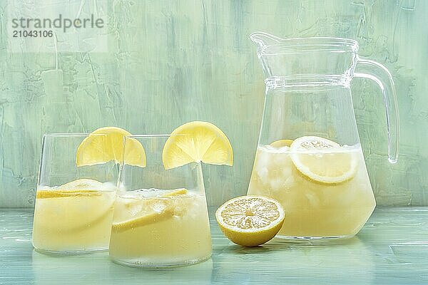 Lemonade. Lemon water drink with ice. Two glasses and a pitcher on a blue background. Detox beverage. Fresh homemade cocktail