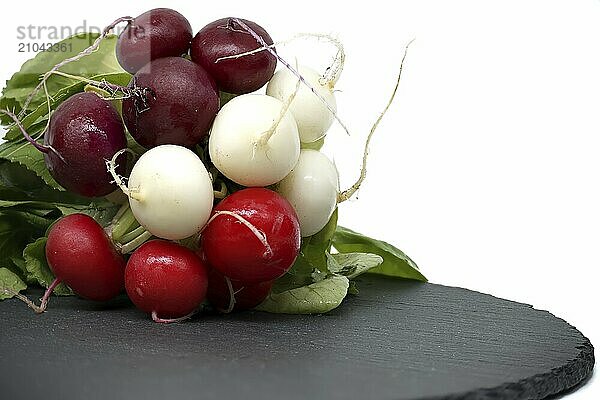 Fresh radish with leaves on black slate serving plate over white background. European radishes (Raphanus sativus)