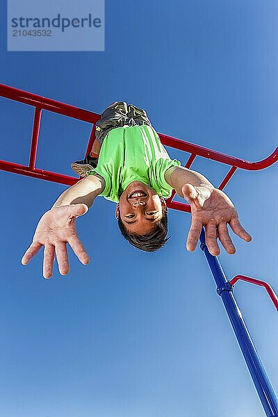 A happy young boy hangs upside down from the monkey bars