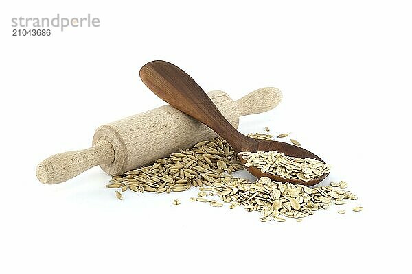 Oats grains with hulls or husks near wooden rolling pin and oats groats rolled and flattened into flakes in wooden spoon isolated on white background