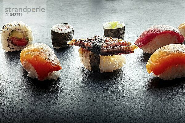 Sushi on a black slate plate. Nigiri with eel  salmon and tuna  roll with avocado and maki with cucumber on a black background  Japanese food on a plate at an Asian restaurant  Food photography  Food photography