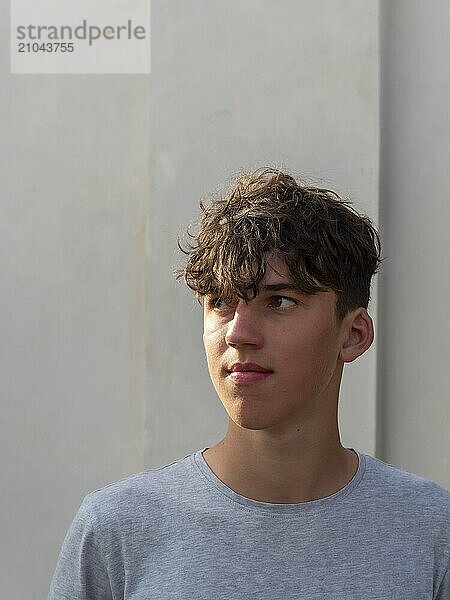 Portrait of a young athletic man with curly brown hair in front of a grey wall  looking into the distance