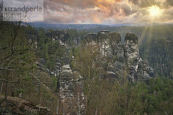 Jagged rocks at the Basteibridge. Wide view over trees and mountains. Dramatic sky. National park in Germany