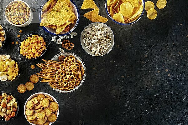 Salty snacks  party mix  shot from the top with copy space. An assortment of appetizers  a flat lay on a black background. Potato and tortilla chips  crackers  popcorn etc  Food photography  Food photography