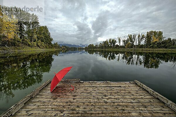 A concept photo of a red umbrella resting on a wooden dock by Kootenai RIver in north Idaho during autumn