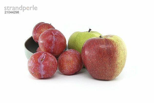 Assortment of fresh fruits set against a white backdrop  including vivid green apples and crimson plums