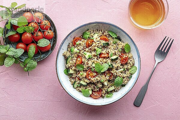 Quinoa tabbouleh salad in a bowl  a healthy dinner with tomatoes and mint  with a fork and a drink  overhead flat lay shot on a pink background  Food photography  Food photography