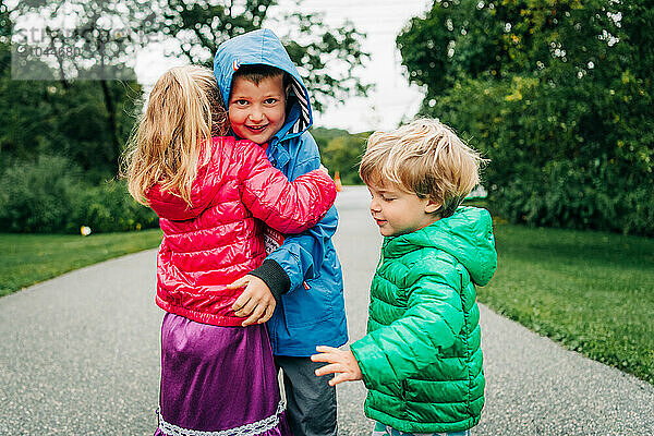 Three children hugging outdoors  dressed in bright jackets