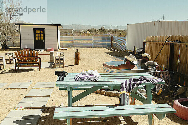 Two men in cowboy hats relaxing in a water tub in a desert backyard.