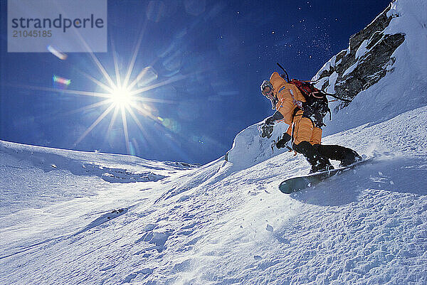 A man snowboards down the North Face of Mount Everest with a sun flare in background.