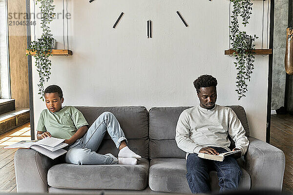 African American father and boy sitting together reading books