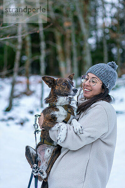 Young woman holding and smiling at cute brown dog on a snow landscape