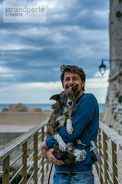 Young man holding brown dog in his arms smiling at the camera