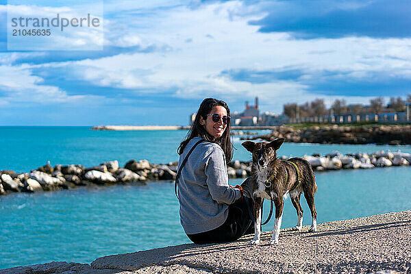 Woman with brown dog looking and smiling to the camera near the sea