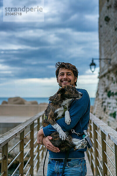 Young man holding brown dog in his arms smiling at the camera