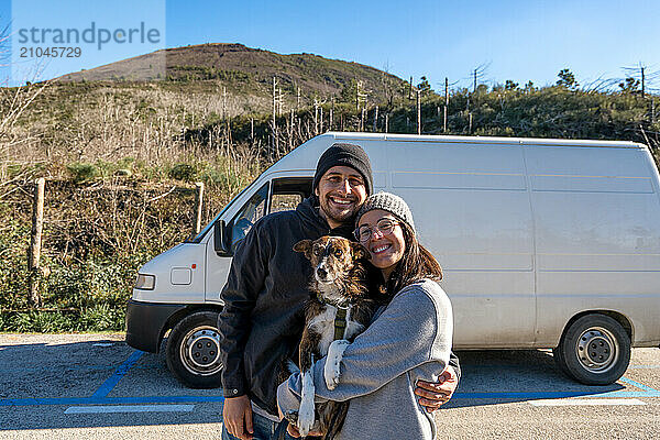 Couple looking and smiling at camera with their dog and a camper van