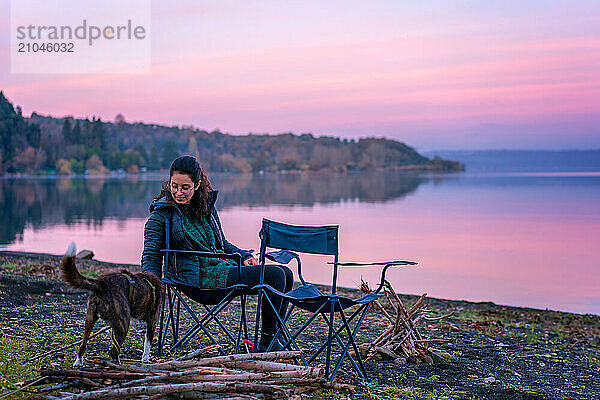 Woman playing with a dog with a wooden stick near a lake at sunset