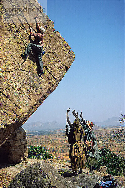 A man climbs on a boulder in the Bandiagara Valley  Mali  as two Dogon villagers spot him.